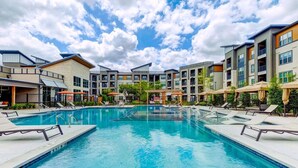 Une piscine entourée de bâtiments à plusieurs étages dotés de balcons, avec des chaises longues et des parasols à proximité.