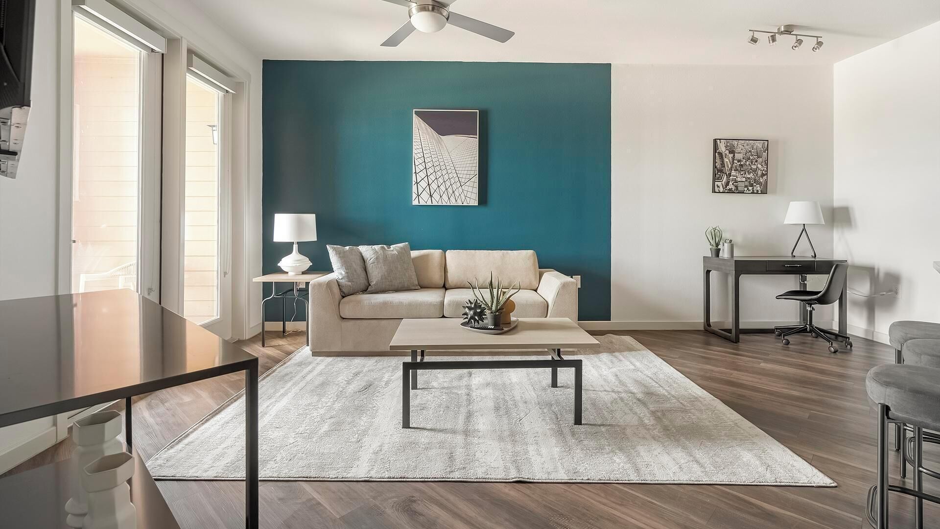 Un salon moderne avec un mur d’accent de couleur turquoise, un canapé beige, une table basse et un bureau avec une chaise.
