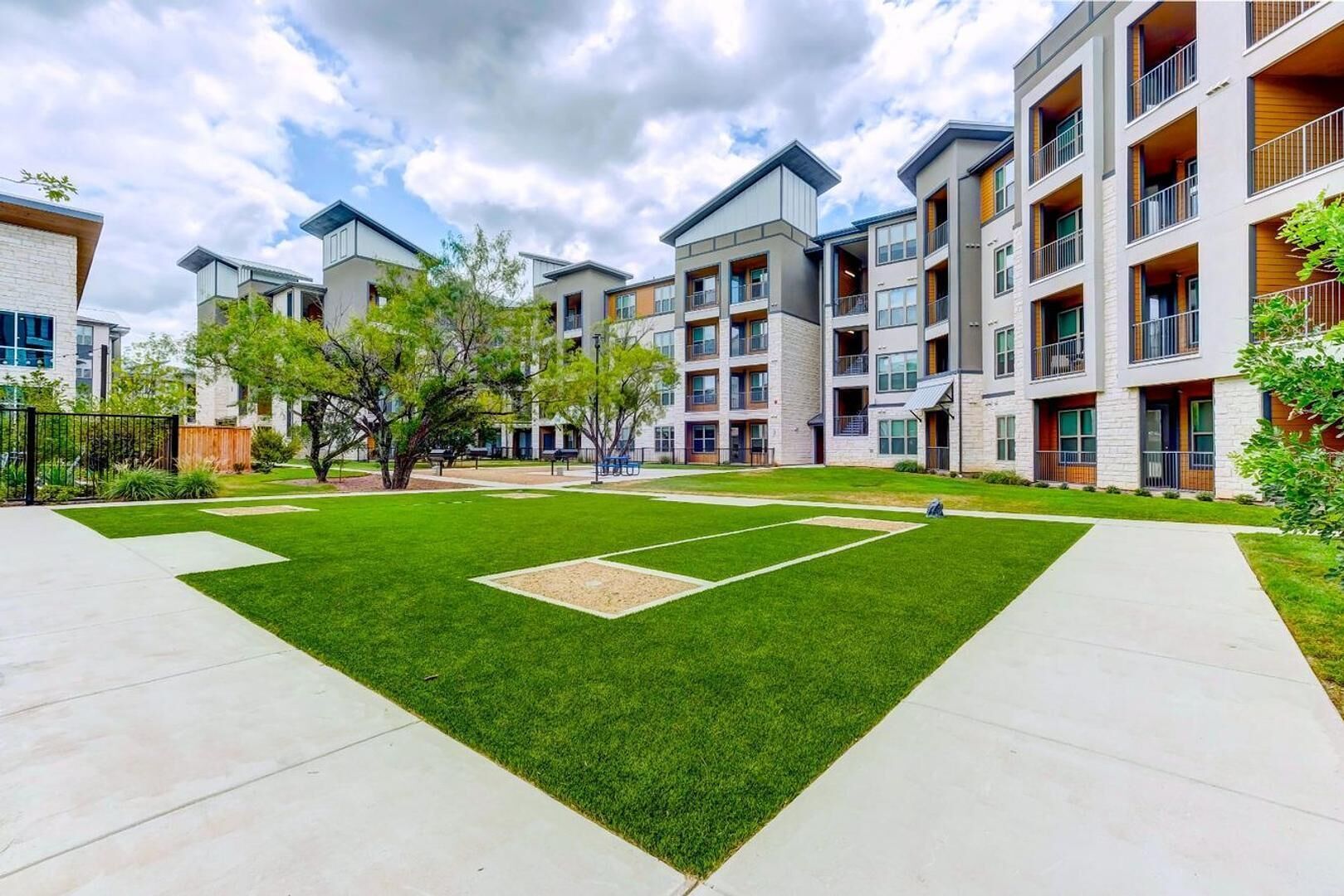 A modern apartment complex with multiple buildings, a well-maintained lawn, and a tennis court.