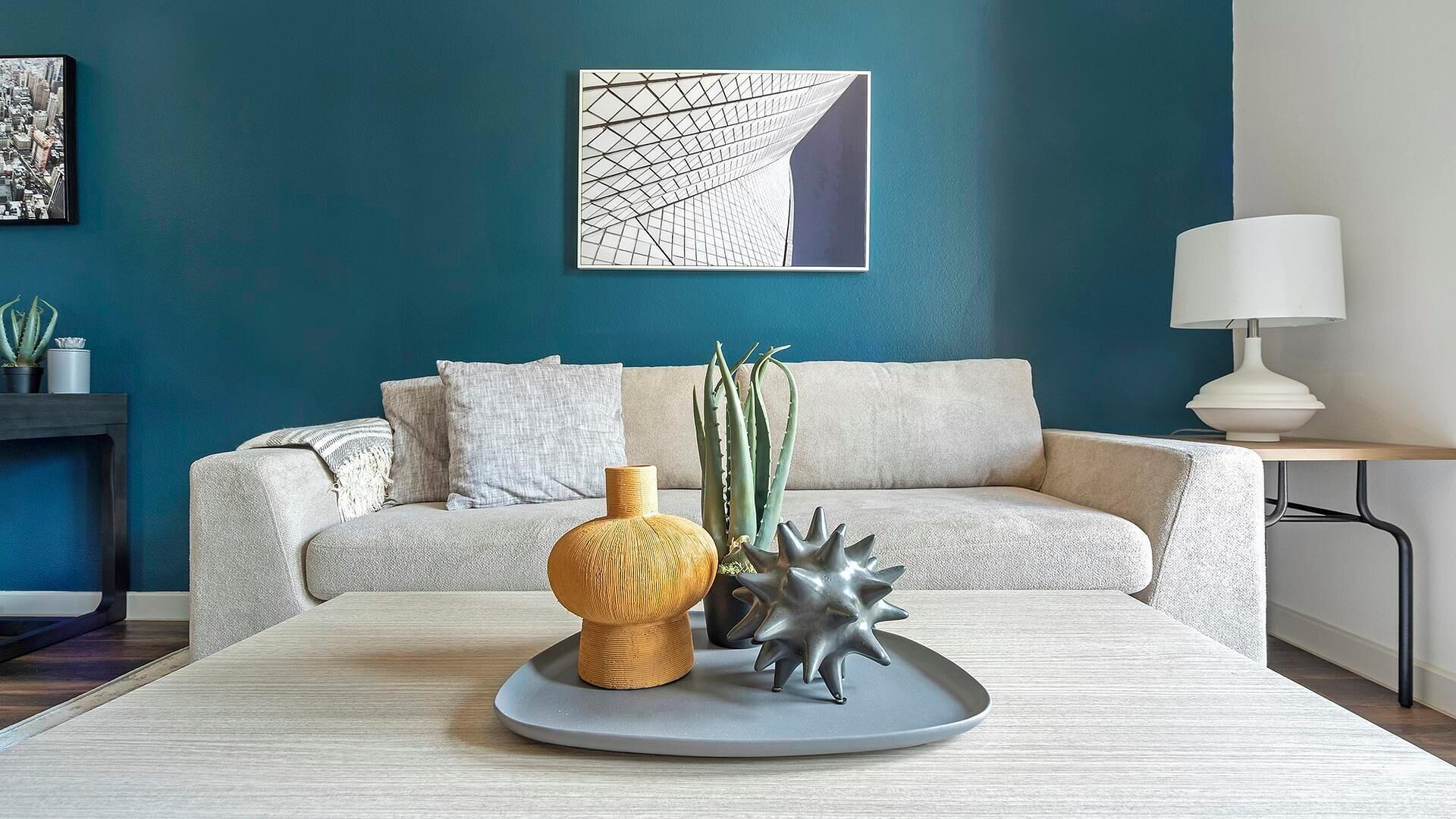A modern living room with a teal accent wall, a grey sofa, a coffee table with decorative items, and a lamp.