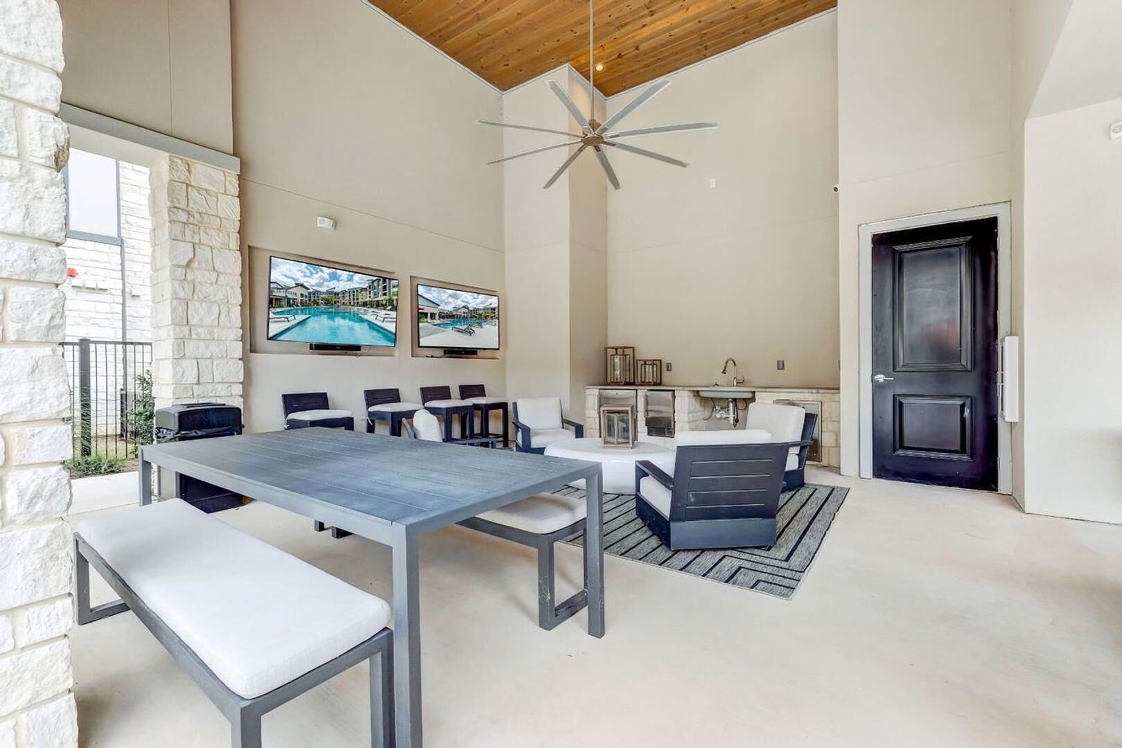 A spacious indoor area with a long table and chairs, a ceiling fan, and a stone wall.