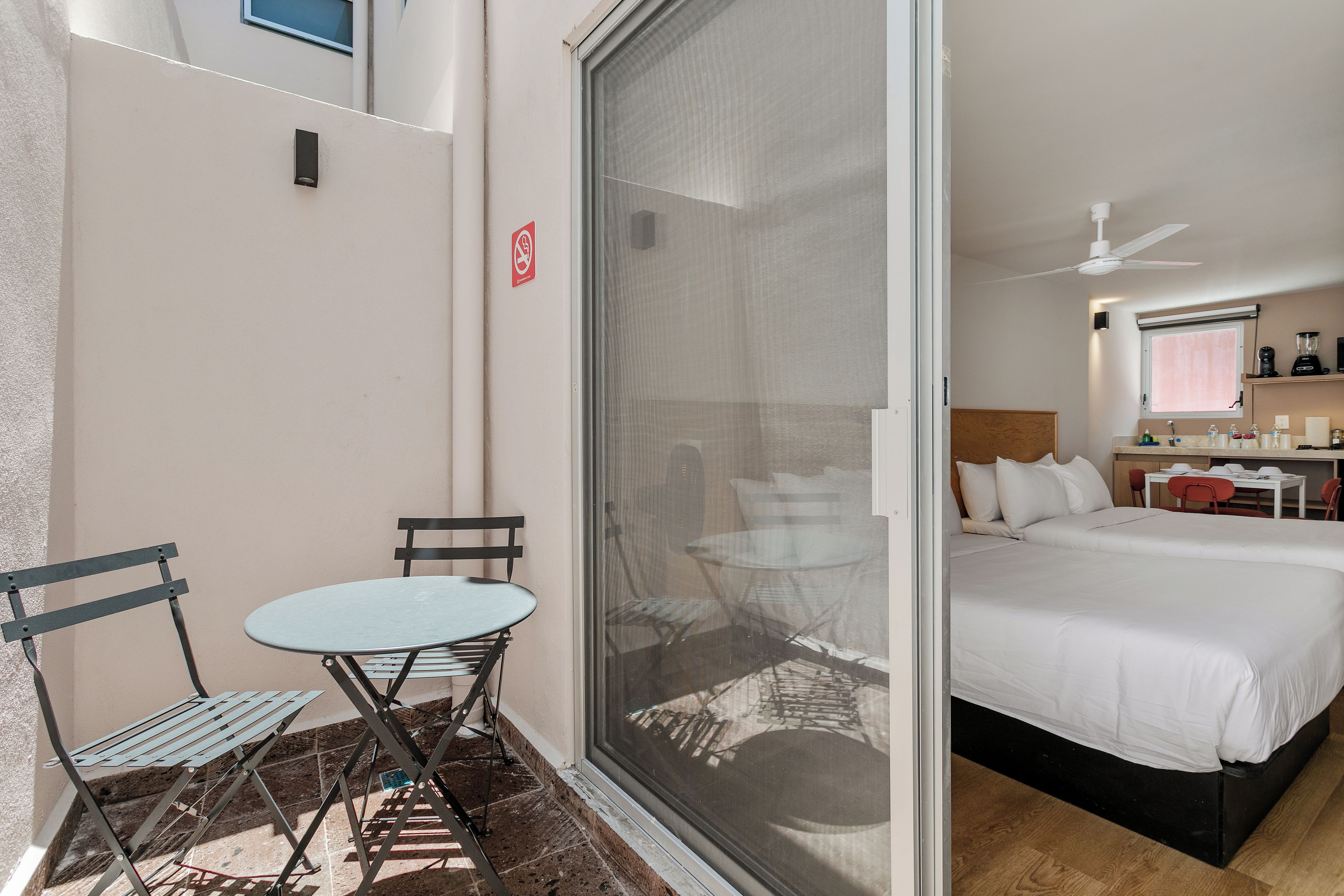 A hotel room with a bed, a small table with chairs, a window with a view, and a balcony with a chair and table.