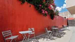 Pared roja con planta trepadora y zona de estar exterior con sillas y mesas de metal.