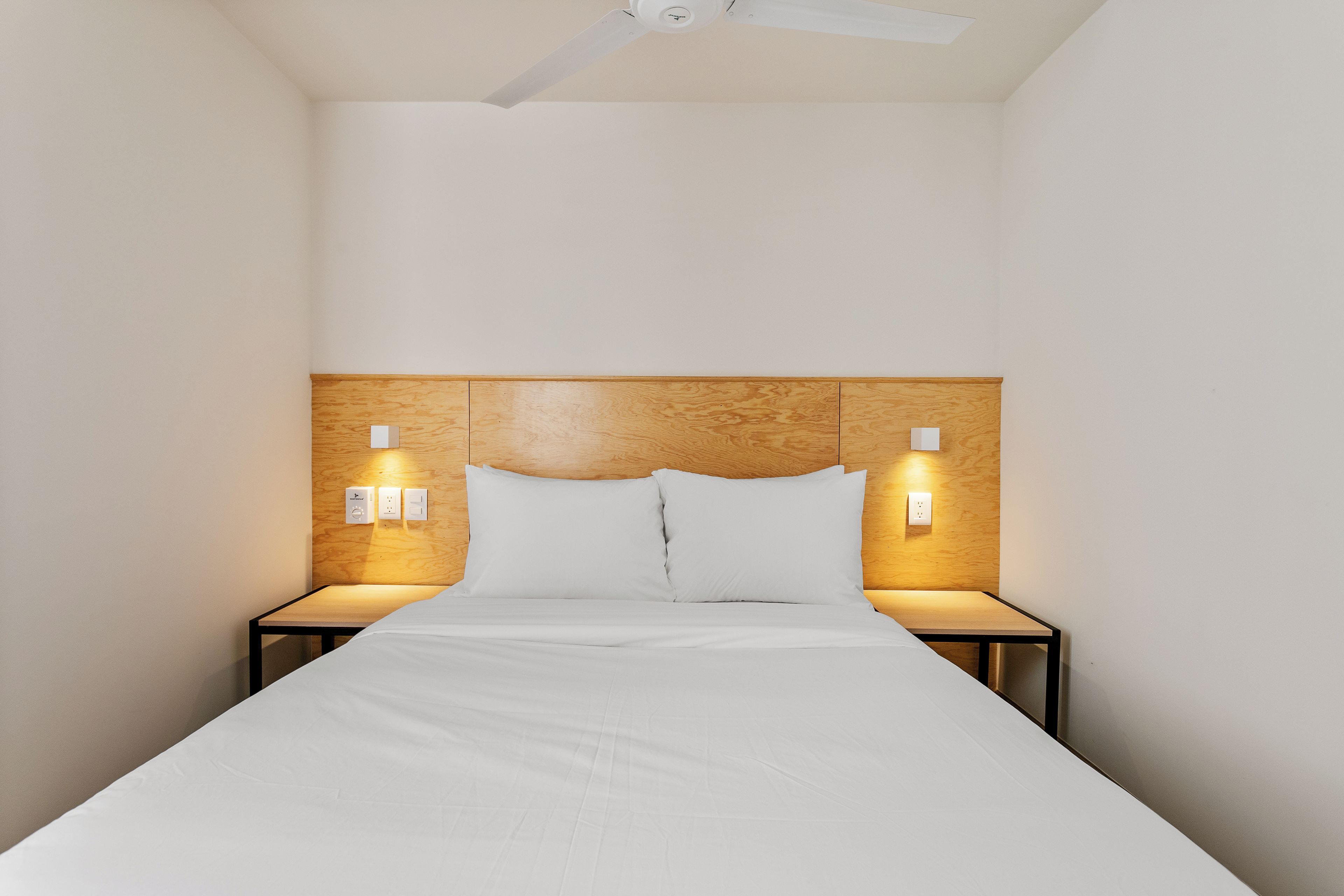 A hotel room with a bed, wooden headboard, bedside lamps, and a ceiling fan.