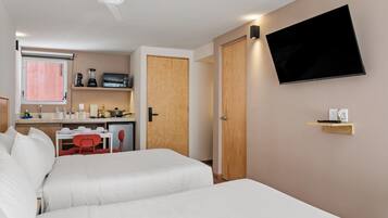 Una habitación de hotel con cama, televisión montada en la pared, kitchenette y ventilador de techo.