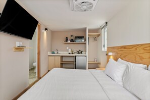 A hotel room with a bed, a TV mounted on the wall, a kitchenette with a microwave, and a small refrigerator.