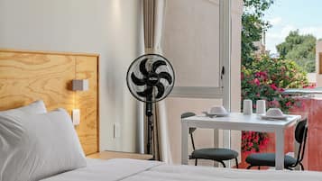 A hotel room with a bed, a table with chairs, a standing fan, and a window with curtains.