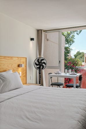 A hotel room with a bed, a table with chairs, a standing fan, and a window with curtains. - Ezequiel Montes By Homirent (Queretaro)