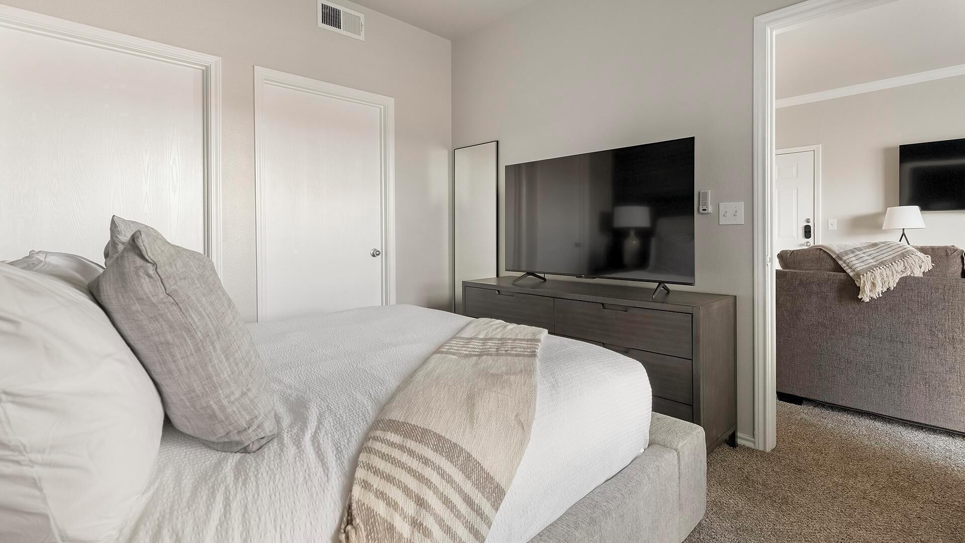 A hotel room with a bed, a dresser, a TV, and a door.