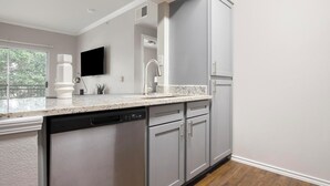 A modern kitchen with grey cabinets, a dishwasher, a sink, and a flat-screen TV mounted above the counter. - Landing | Modern 1BD, Gym, Pool (San Antonio)