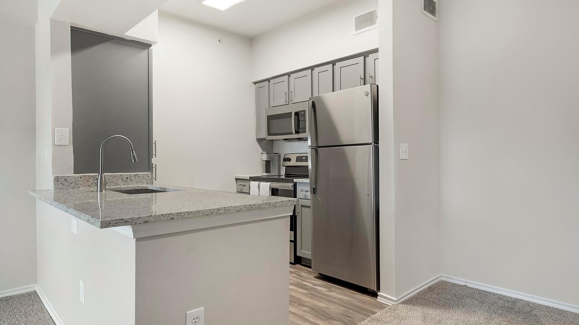 A modern kitchen with a stainless steel refrigerator, microwave, and oven.