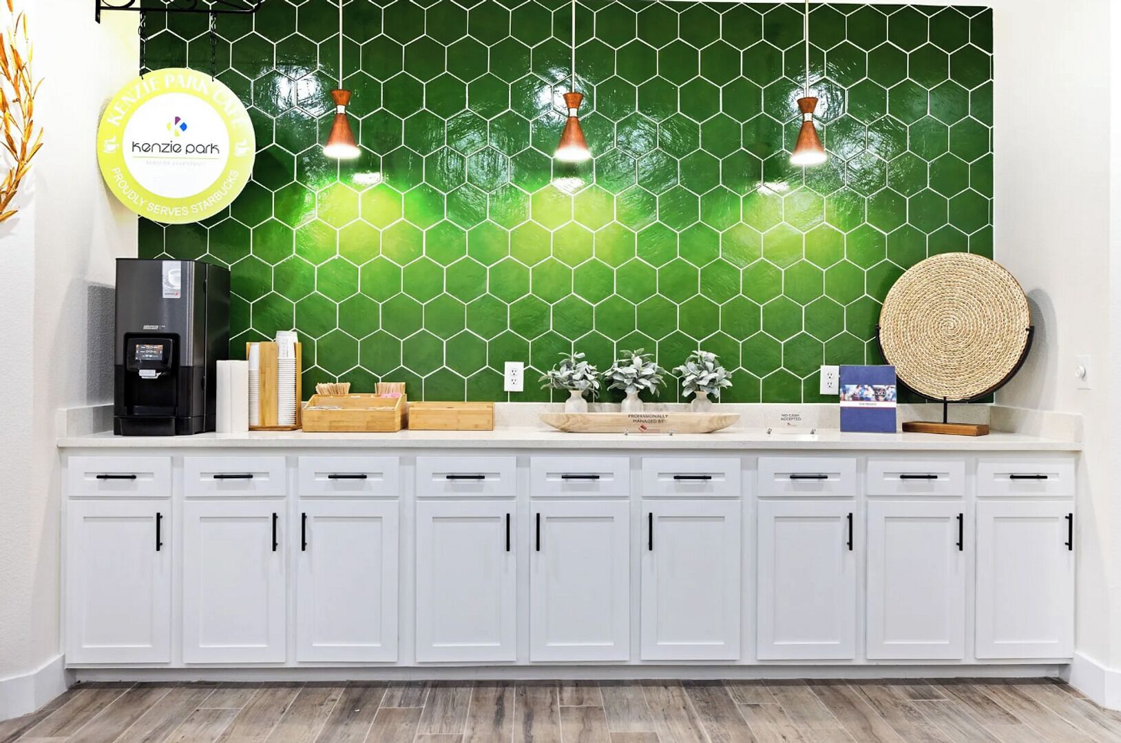 Una encimera de cocina con una cafetera, un cartel de Kenzie Park y un salpicadero hexagonal verde.