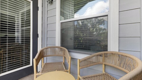 A corner seating area with two wicker chairs and a small round table, adjacent to a window with blinds.