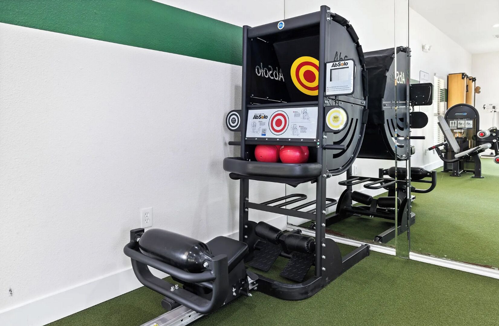 Et træningscenter med en squat-stander, røde vægtbolde og en bænk.