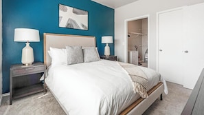 Une chambre à coucher comprenant un lit, des tables de chevet, une tête de lit, un tableau et une armoire.