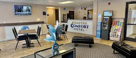Un hall d’hôtel comprenant un comptoir d’accueil, un espace salon et un distributeur automatique de billets.