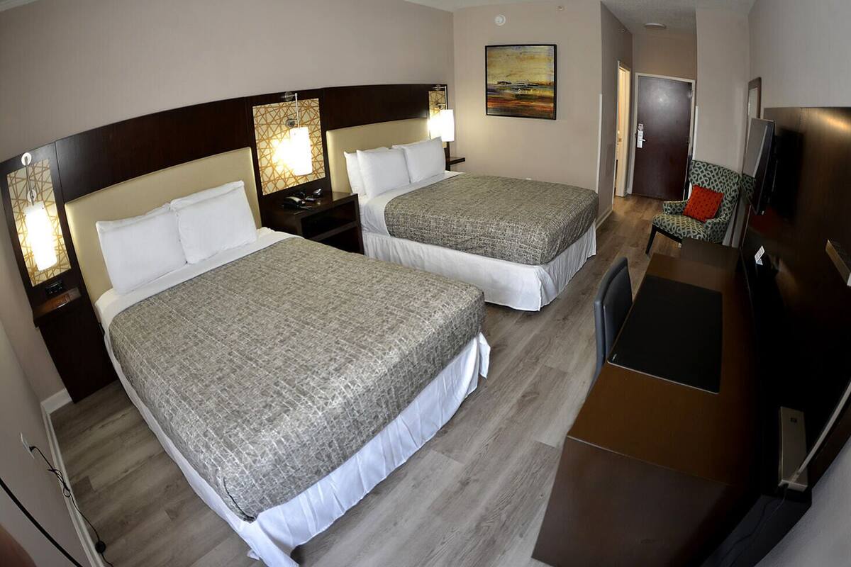 Une chambre d’hôtel avec deux lits, un bureau, une chaise, une télévision et une porte.