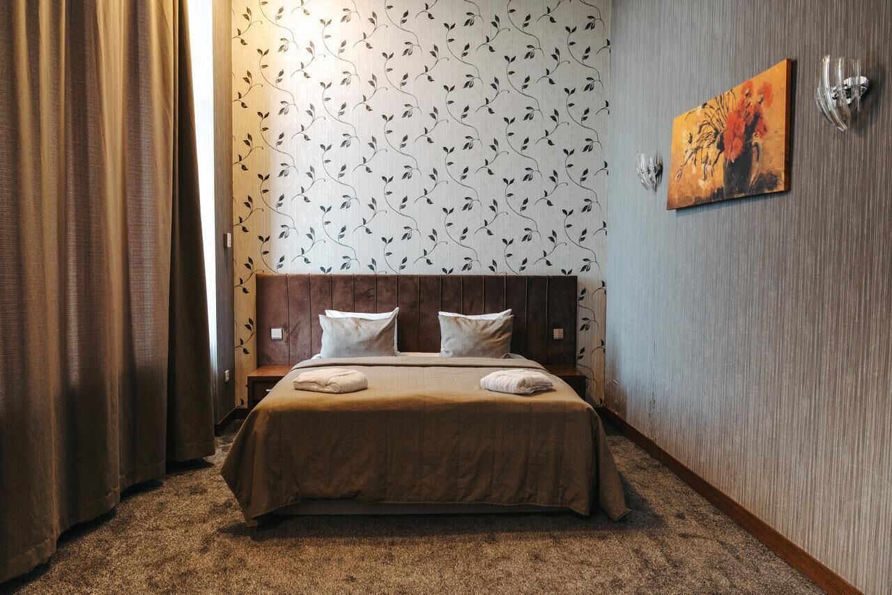 Una habitación de hotel con cabecera de madera, papel tapiz estampado, un cuadro en la pared y suelo alfombrado.