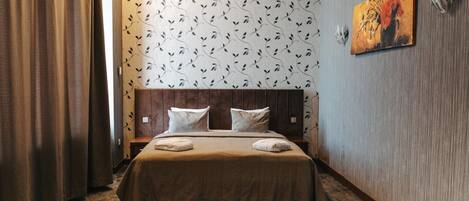 Una habitación de hotel con cabecera de madera, papel tapiz estampado, un cuadro en la pared y suelo alfombrado.