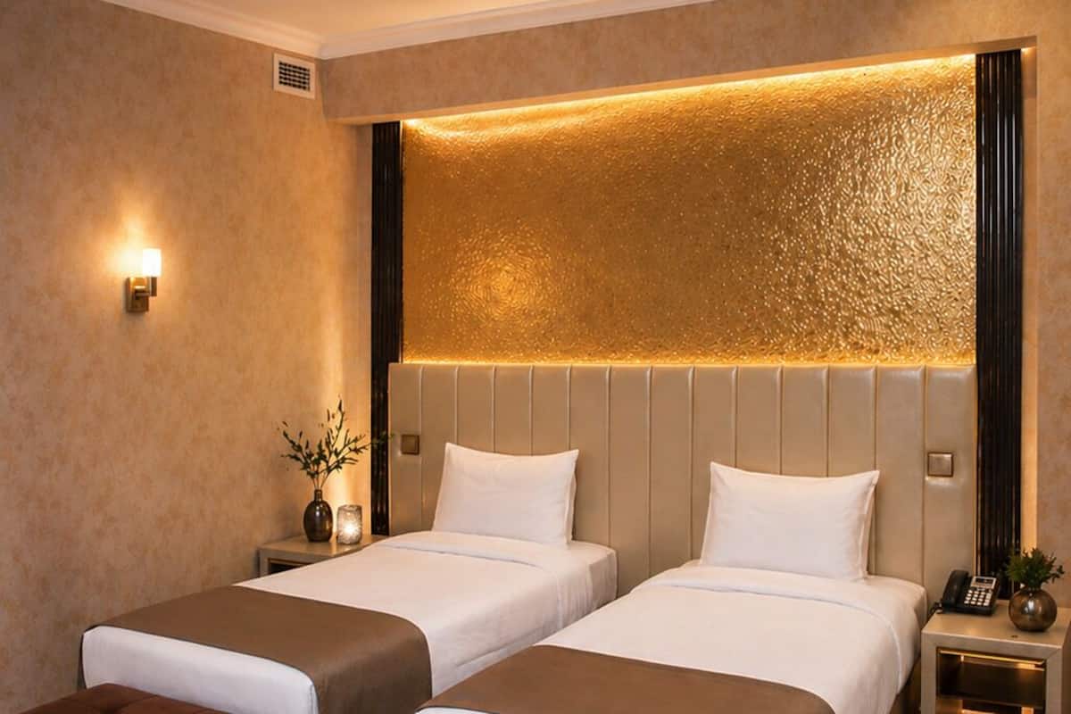 A hotel room with two beds, a sofa, a nightstand, a lamp, and a decorative wall panel.