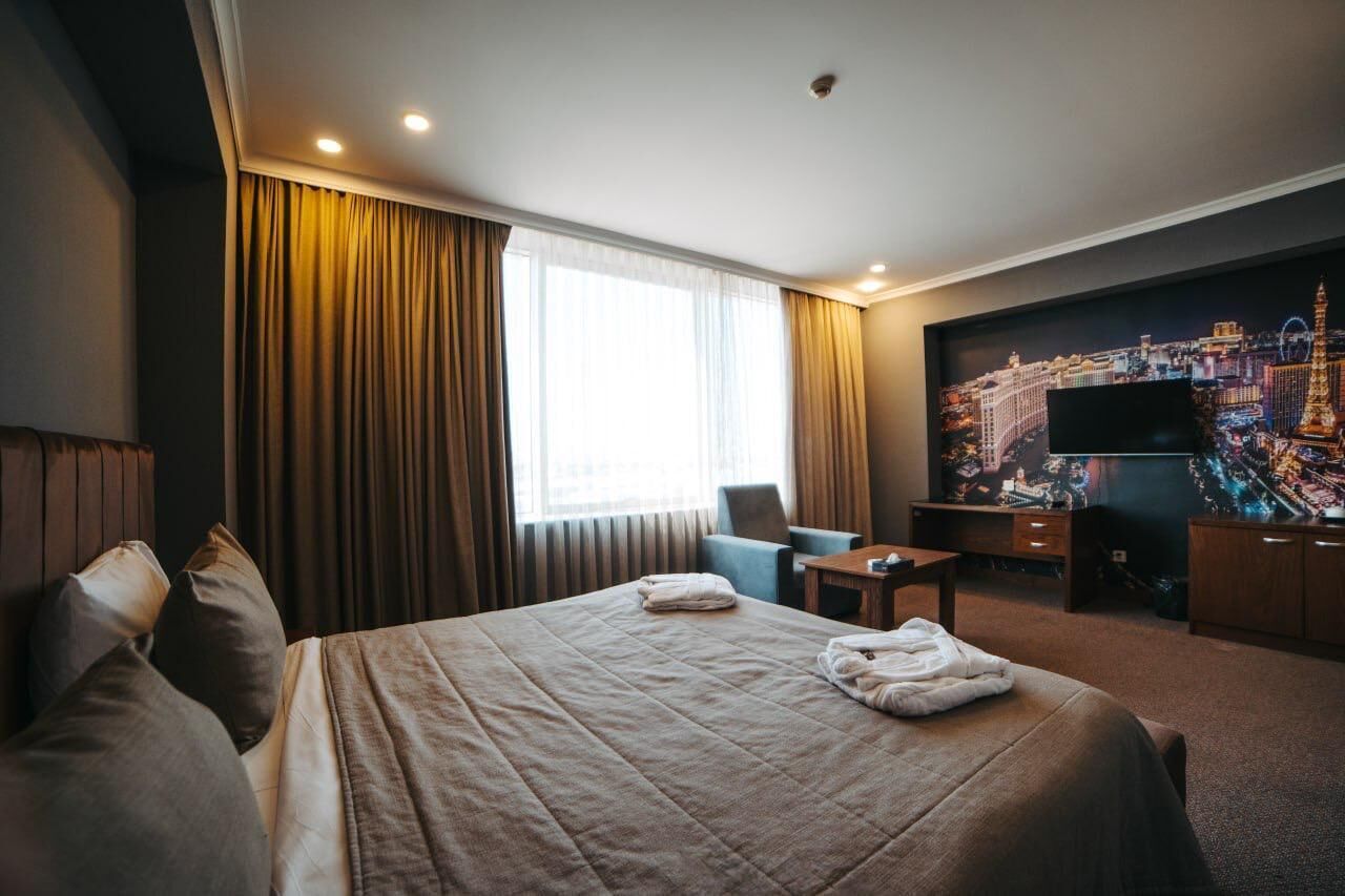 A hotel room with a large bed, a desk, a chair, a television, and a window with curtains.