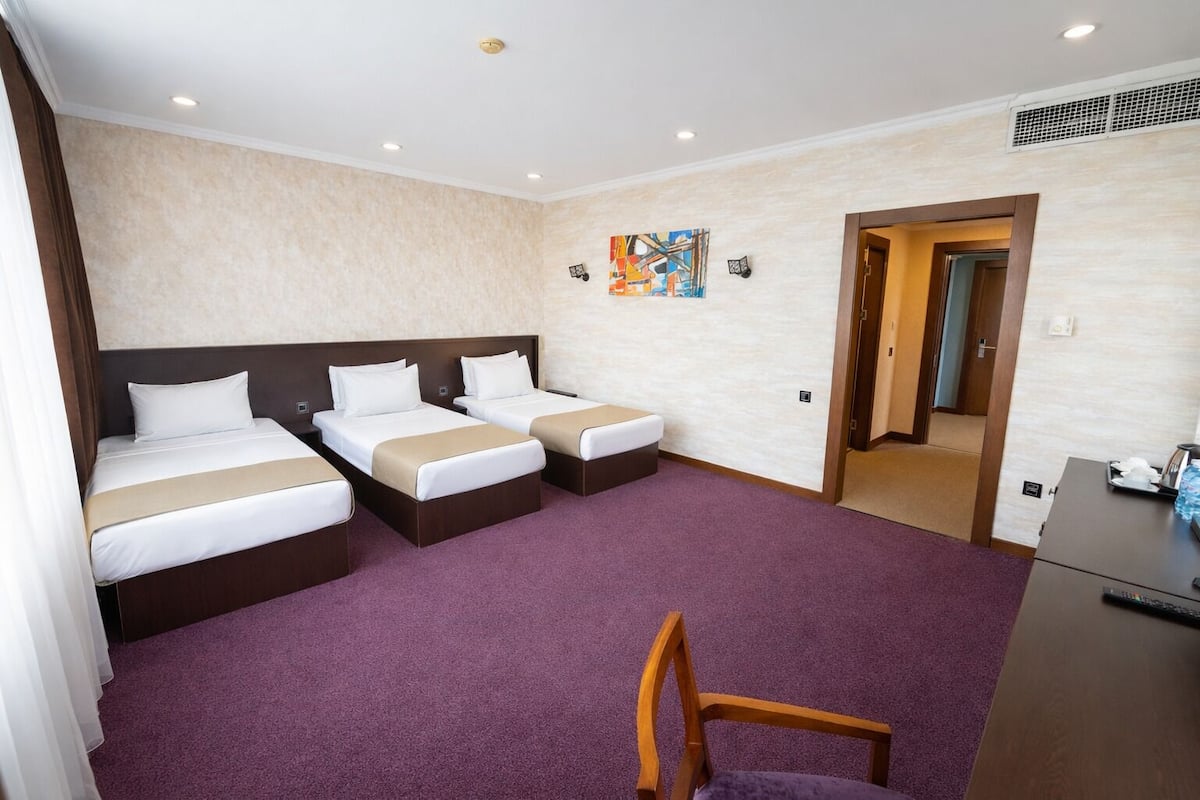 A hotel room with two beds, a desk, a chair, and a door leading to another room.