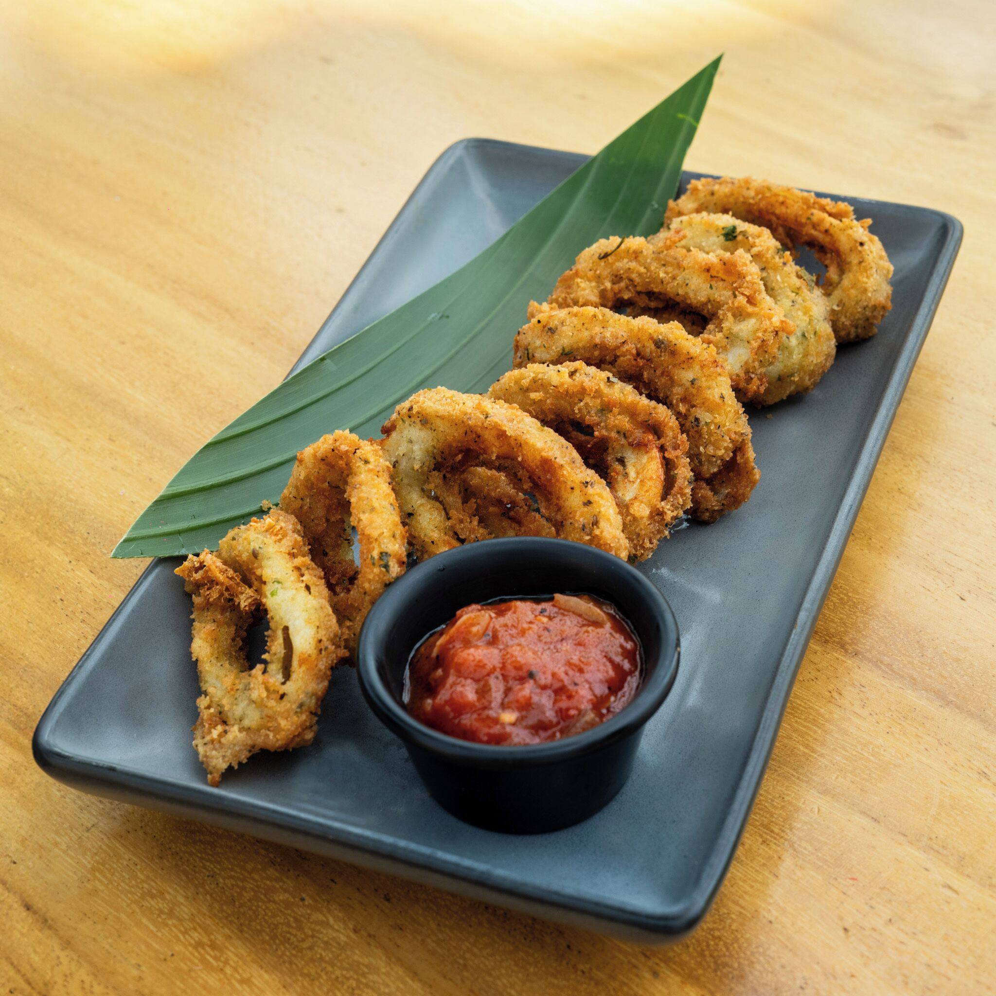 A rectangular plate with fried food items and a small bowl of sauce.