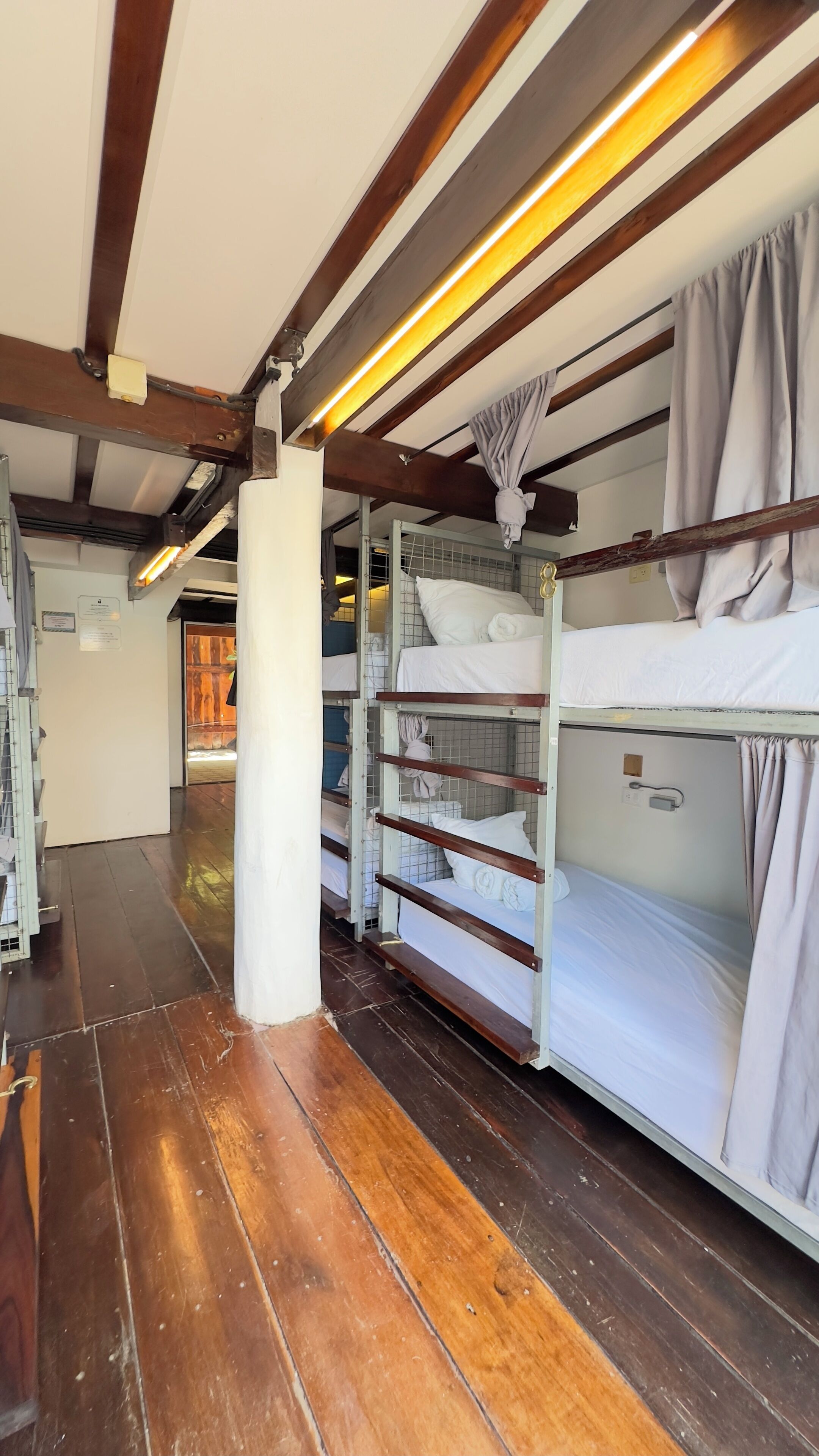 Un couloir avec des lits superposés, des poutres en bois et un éclairage vif au plafond.