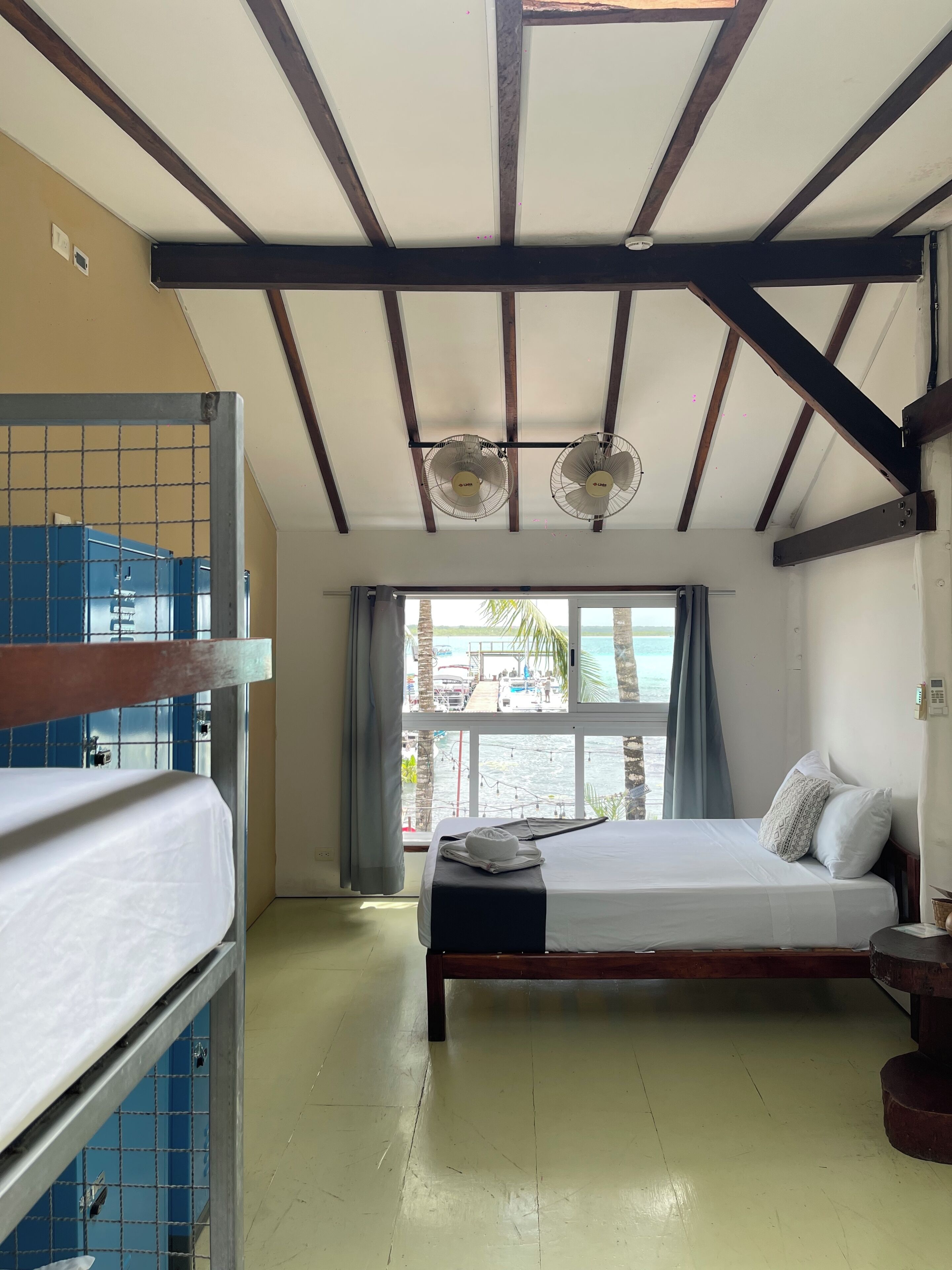 A room with a bunk bed, a single bed, a ceiling fan, and a window with a view of the sea.