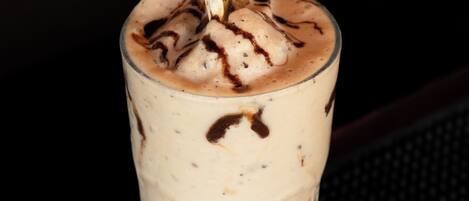 A glass of layered beverage with chocolate syrup on a dark surface.