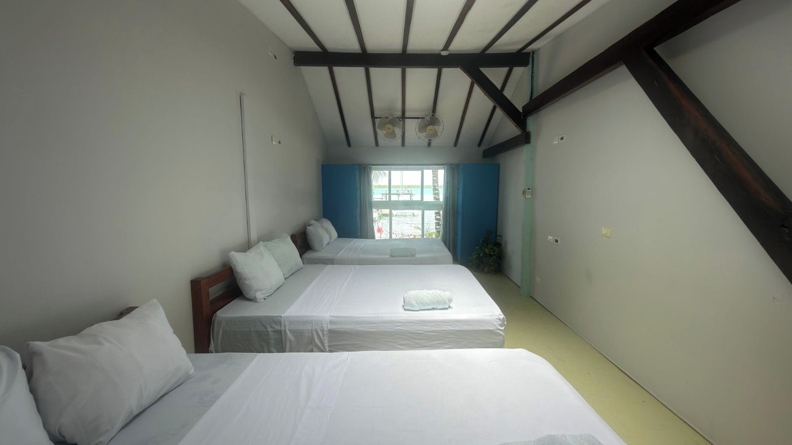 A room with two beds, a ceiling fan, and a window with curtains.