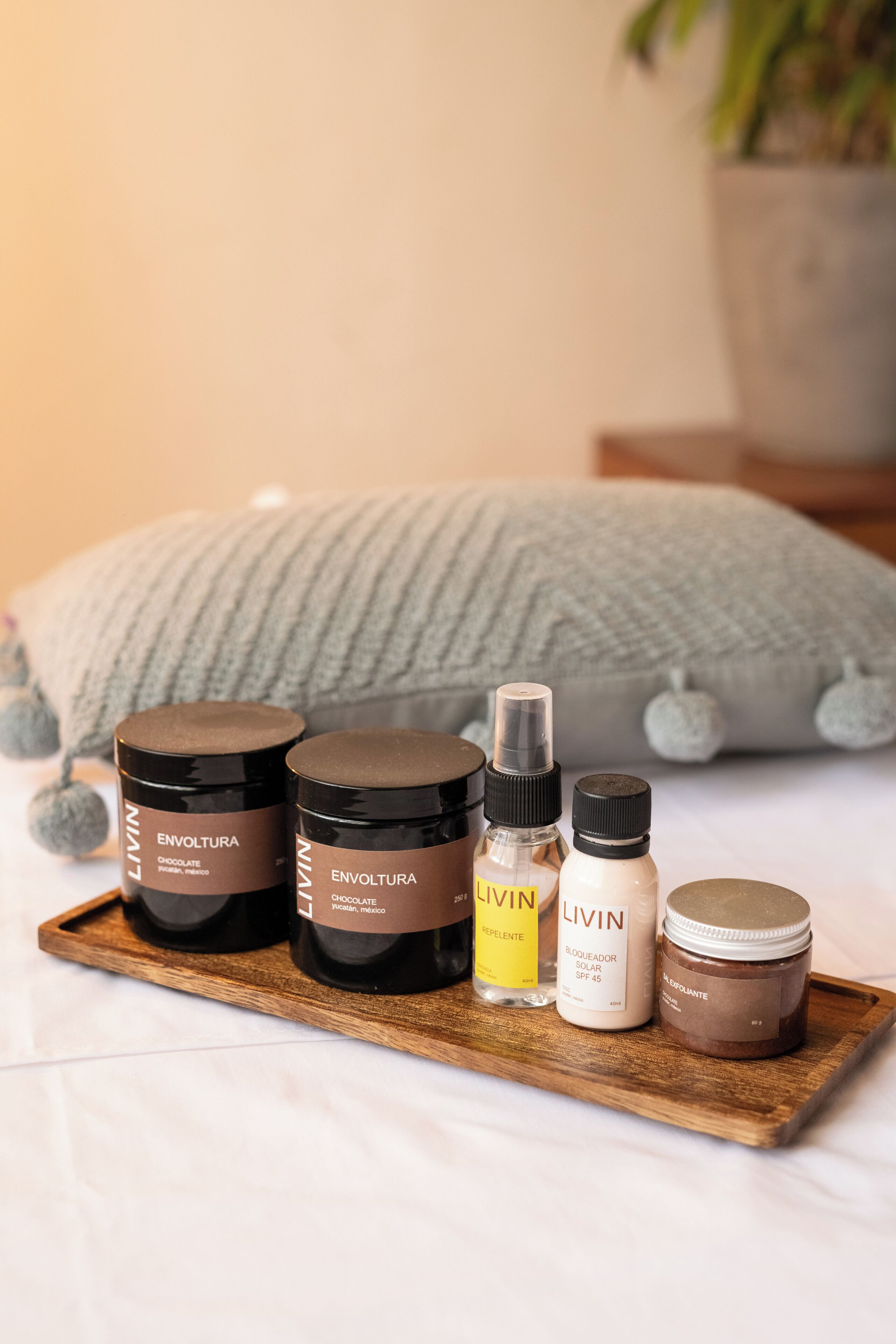 A wooden tray with various L'ININ skincare products, including a chocolate body scrub, a repellent, a sunscreen, and a exfoliating cream.