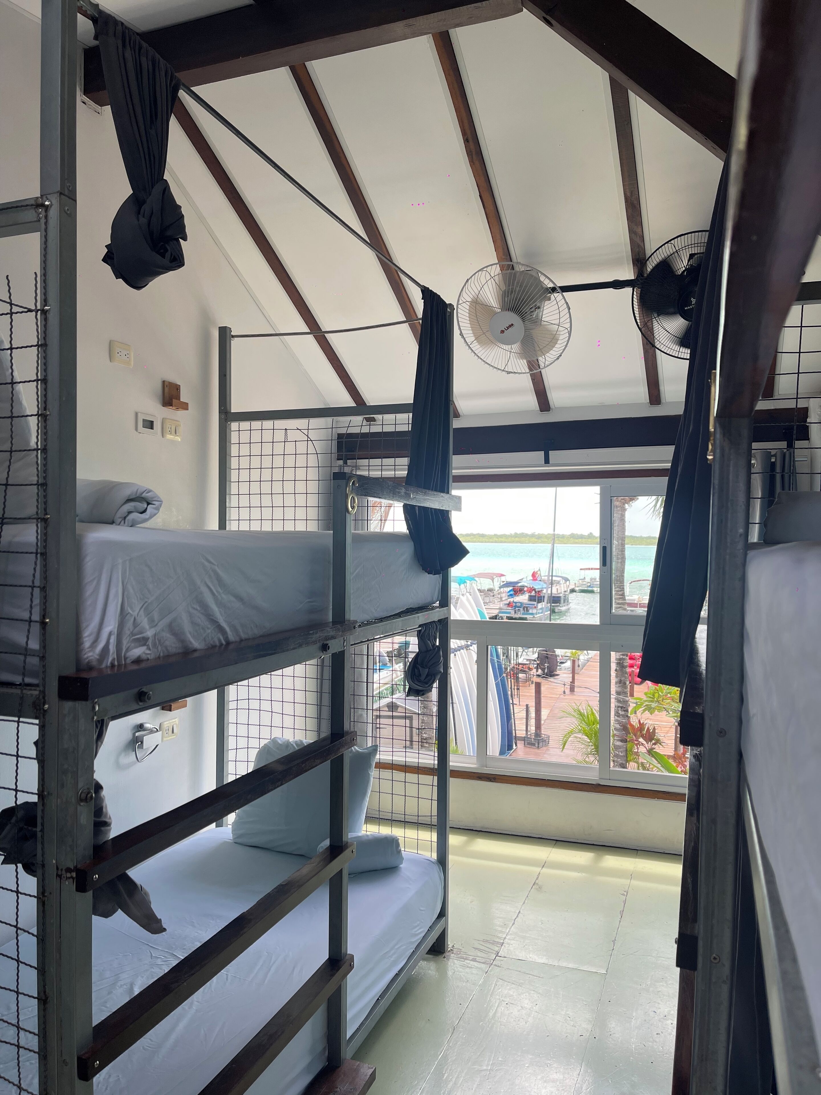 Un dormitorio con literas, ventilador de techo y ventana con vistas a la playa.
