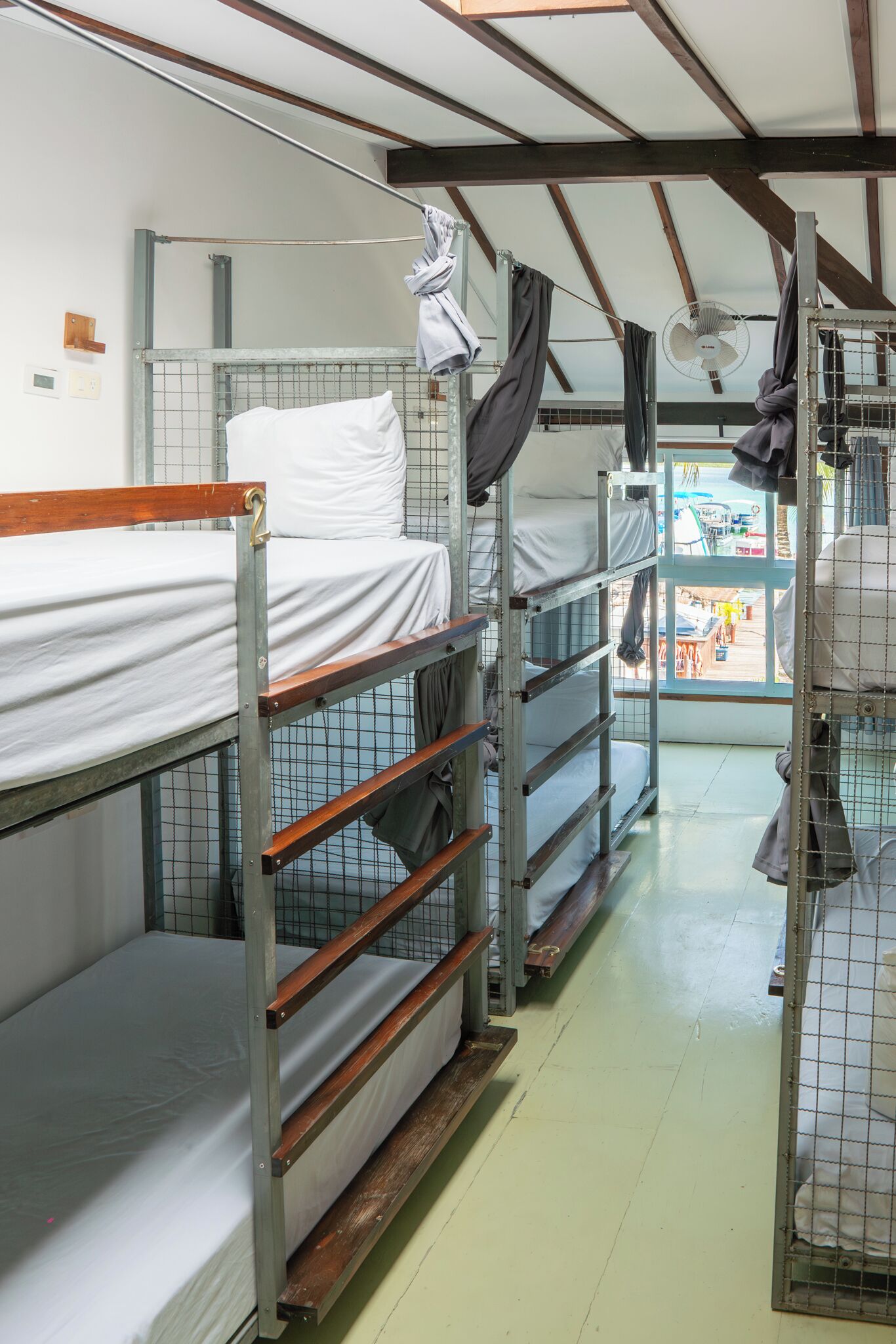 A dormitory-style room with bunk beds, a fan, and a view of the outside.