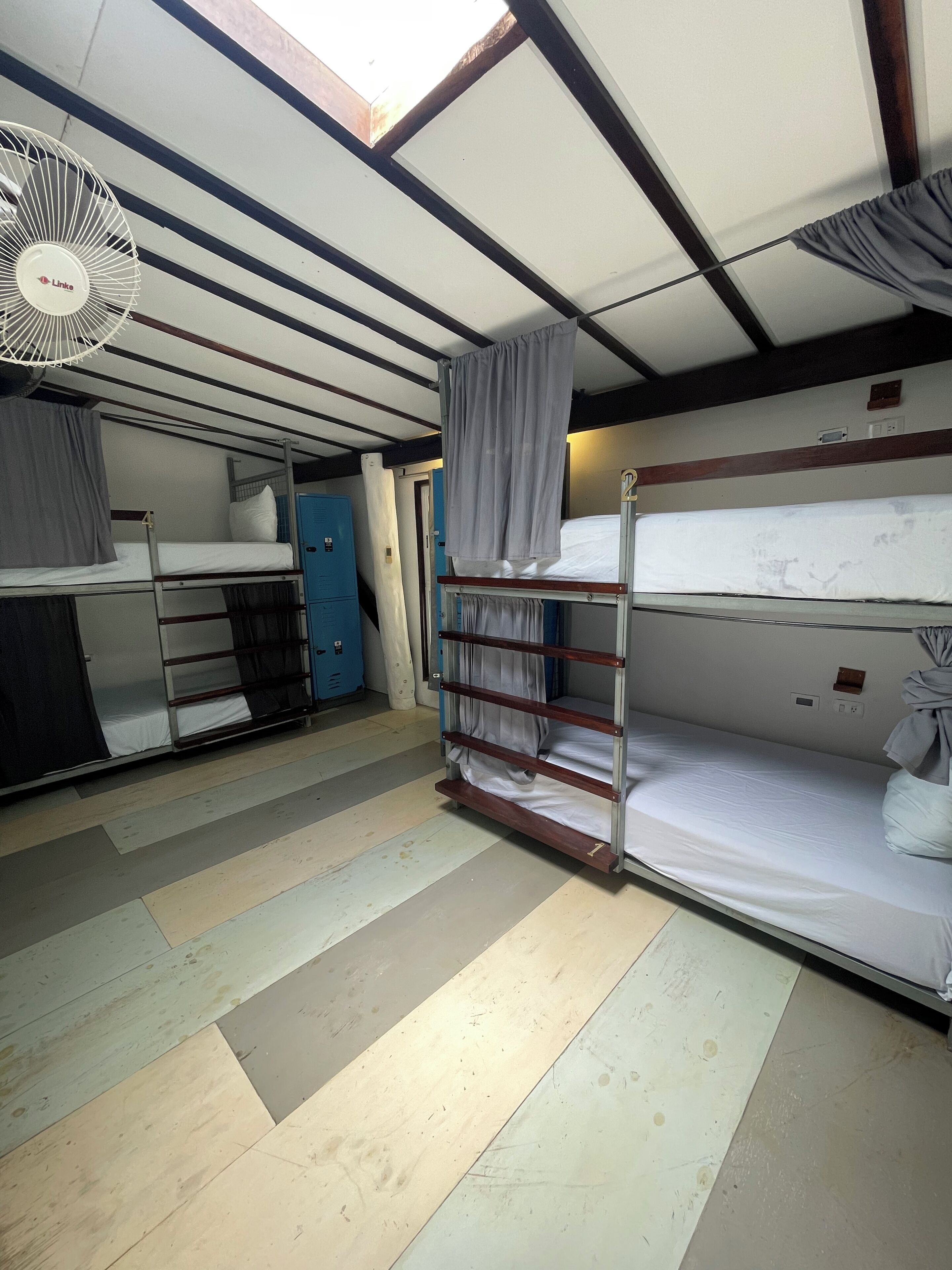 A bunk room with a ceiling fan, a window with curtains, a door, and a small kitchenette area.