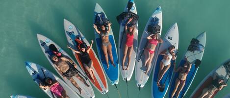 Un grupo de personas descansando sobre tablas de surf en un círculo sobre una masa de agua turquesa.