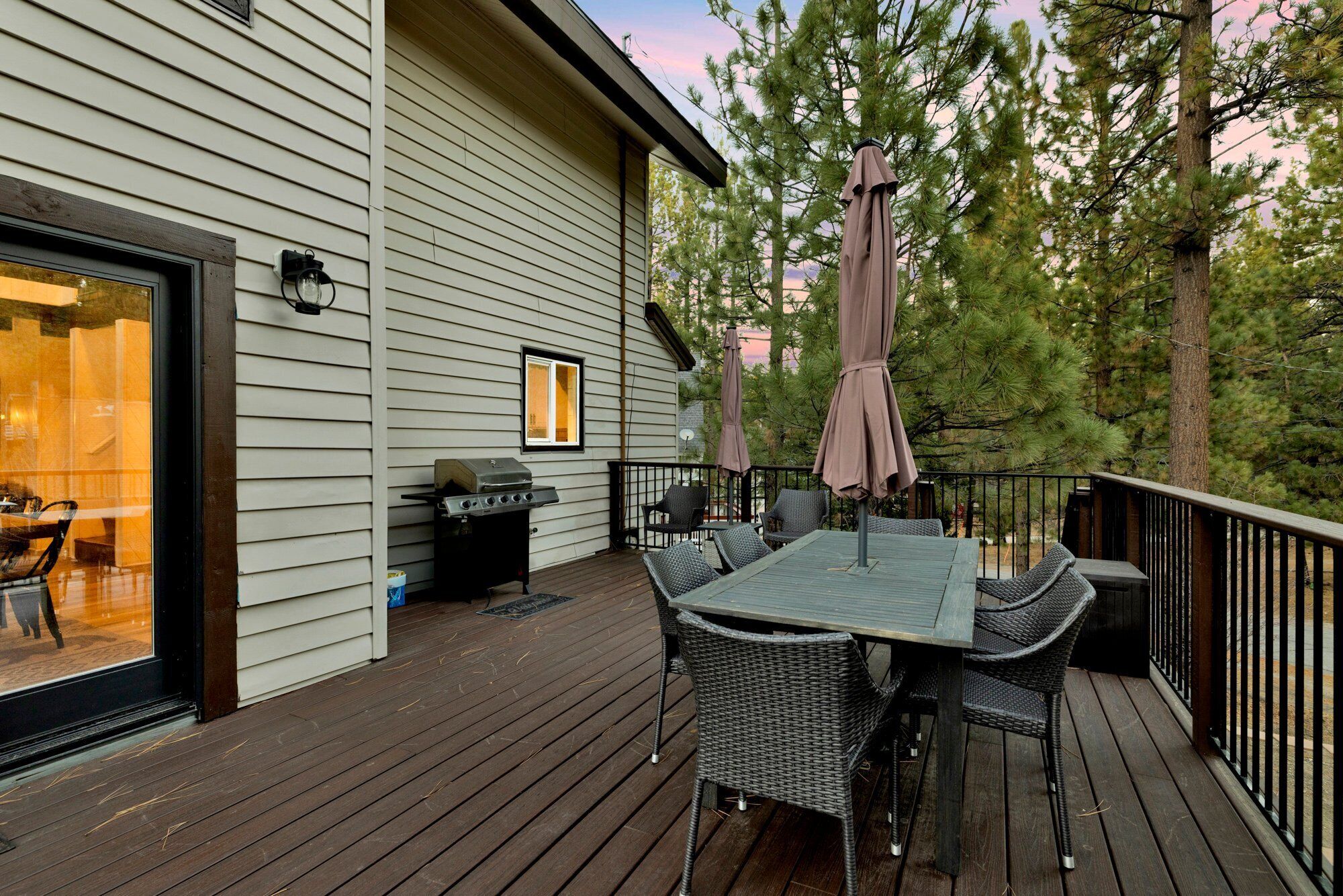 A deck with a table and chairs, a grill, and umbrellas.