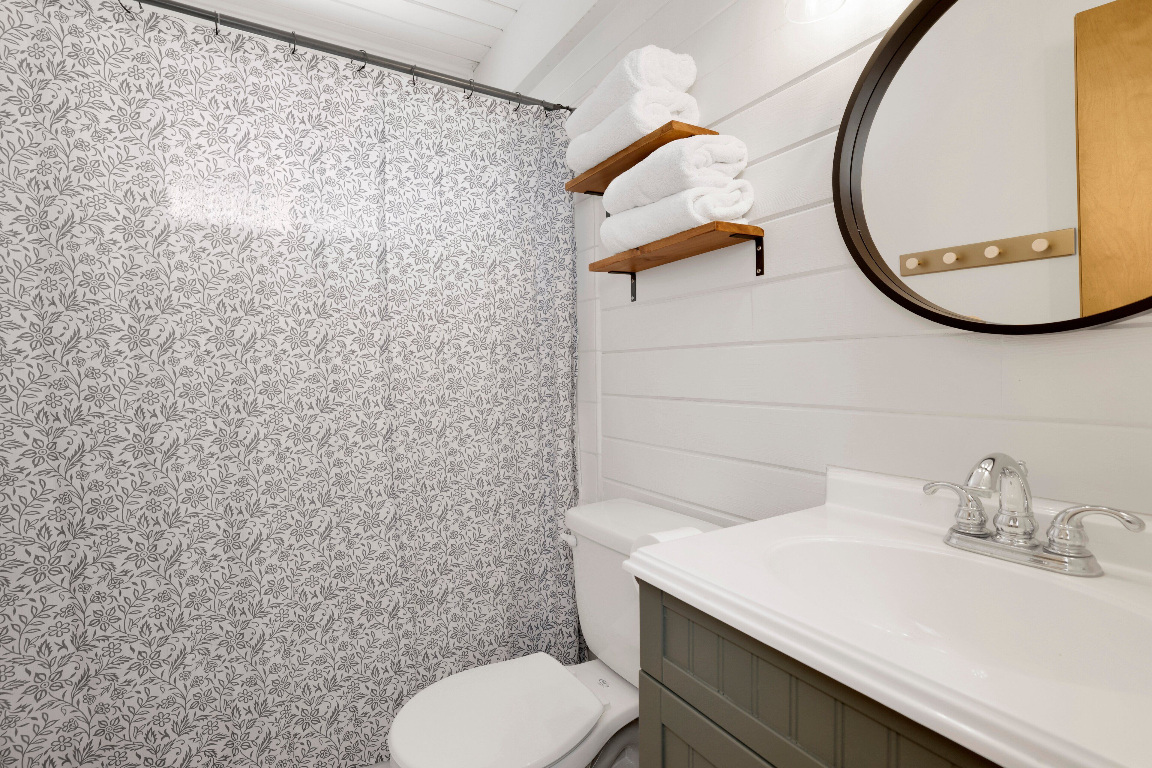 Une salle de bain avec un mur de douche orné de motifs, des toilettes, un lavabo avec un miroir et des porte-serviettes en bois.