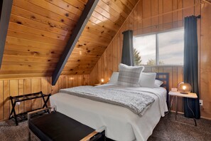 A wooden-paneled room with a bed, a bench, and a window with curtains. - Big Bear Bungalow #643 (Big Bear City)