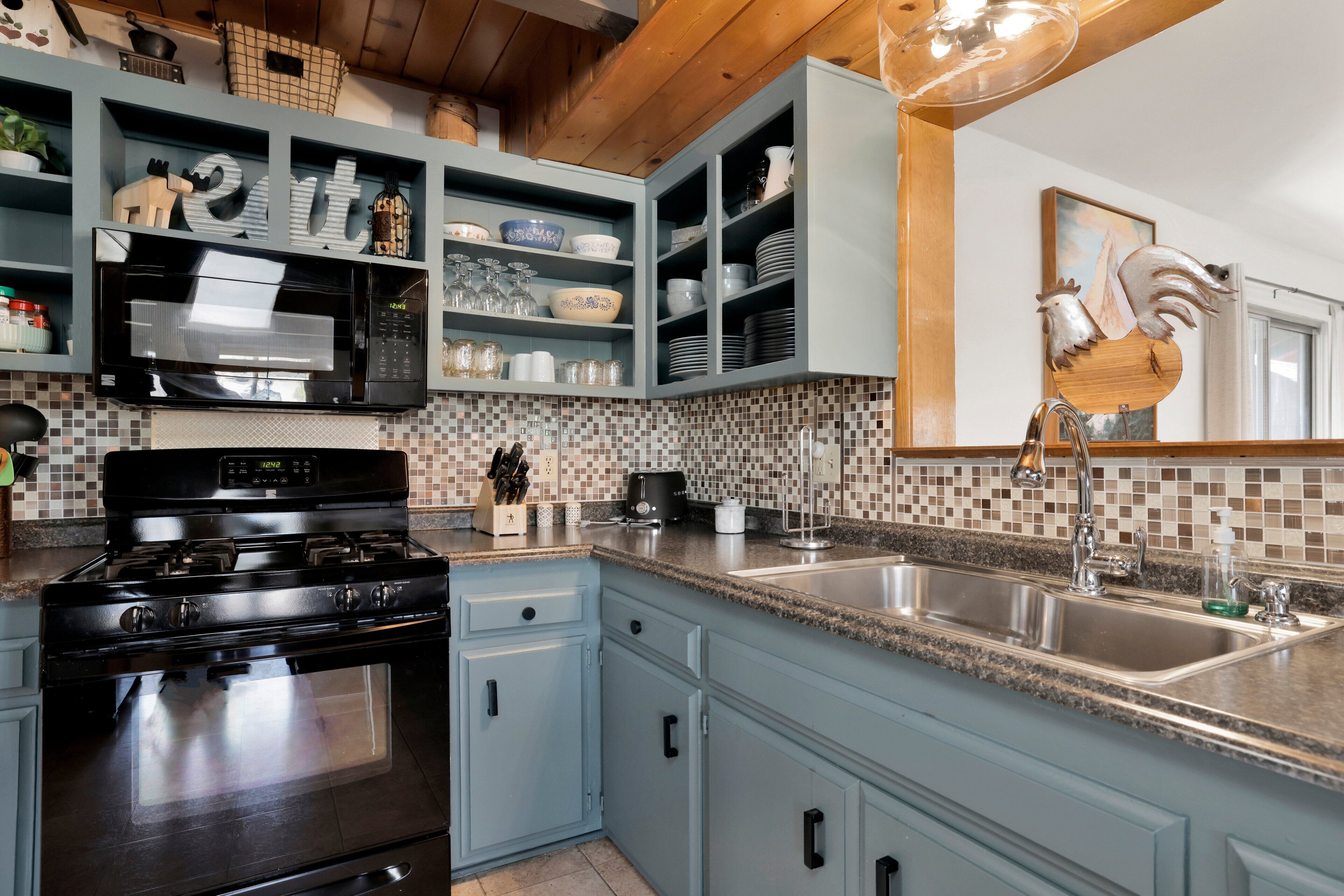 Una cocina con gabinetes azul claro, una estufa negra, un salpicadero de azulejos y un lavamanos con grifo.