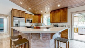 A modern kitchen with wooden cabinets, stainless steel appliances, and a large island with bar stools. - Big Bear White Skies #674 (Big Bear Lake)