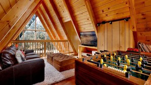 A cozy loft bedroom with a wooden ceiling, a sofa, a futsal table, and a large window offering a view of the outdoors. - Black Diamond Vista #653 (Big Bear Lake)