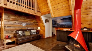 A cozy cabin interior with a wooden interior, a leather sofa, a fireplace, and a television. - Black Diamond Vista #653 (Big Bear Lake)