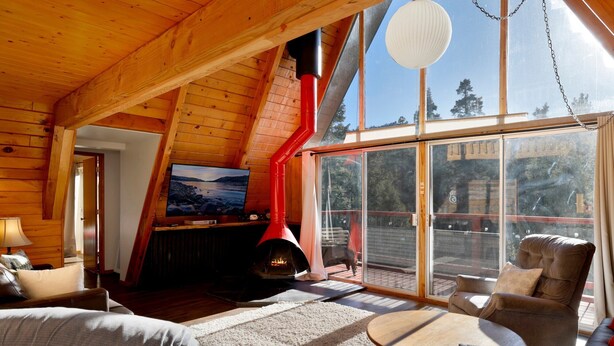 A cozy cabin interior with a fireplace, a TV, and a large window overlooking a scenic landscape. - Black Diamond Vista #653 (Big Bear Lake)