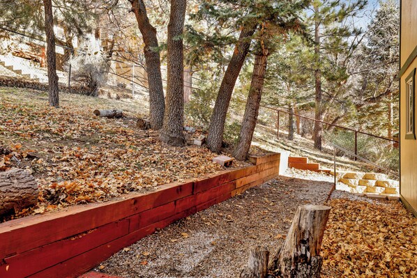 Une terrasse en bois bordée de rouge, entourée d’arbres et d’un chemin de gravier.