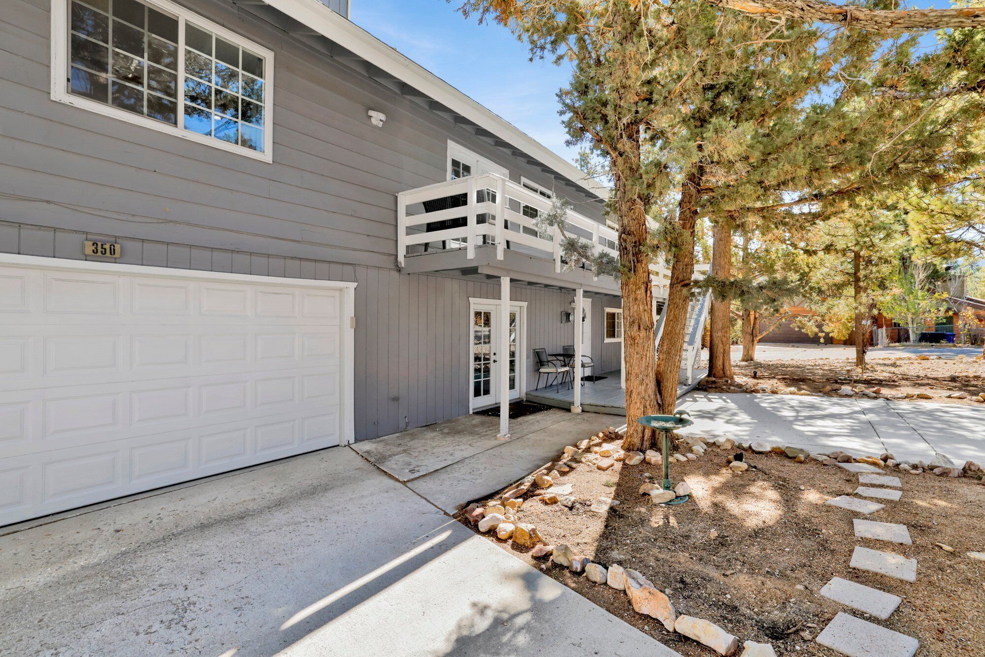 Une maison à deux étages avec une porte de garage blanche, un patio couvert et un chemin en pierre.