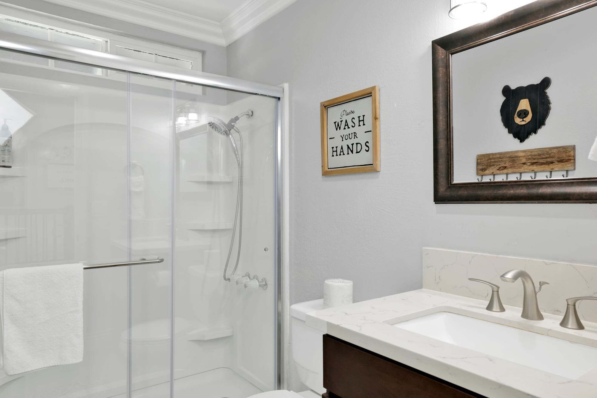A bathroom with a glass shower enclosure, a sink with a marble countertop, and a framed bear artwork on the wall.