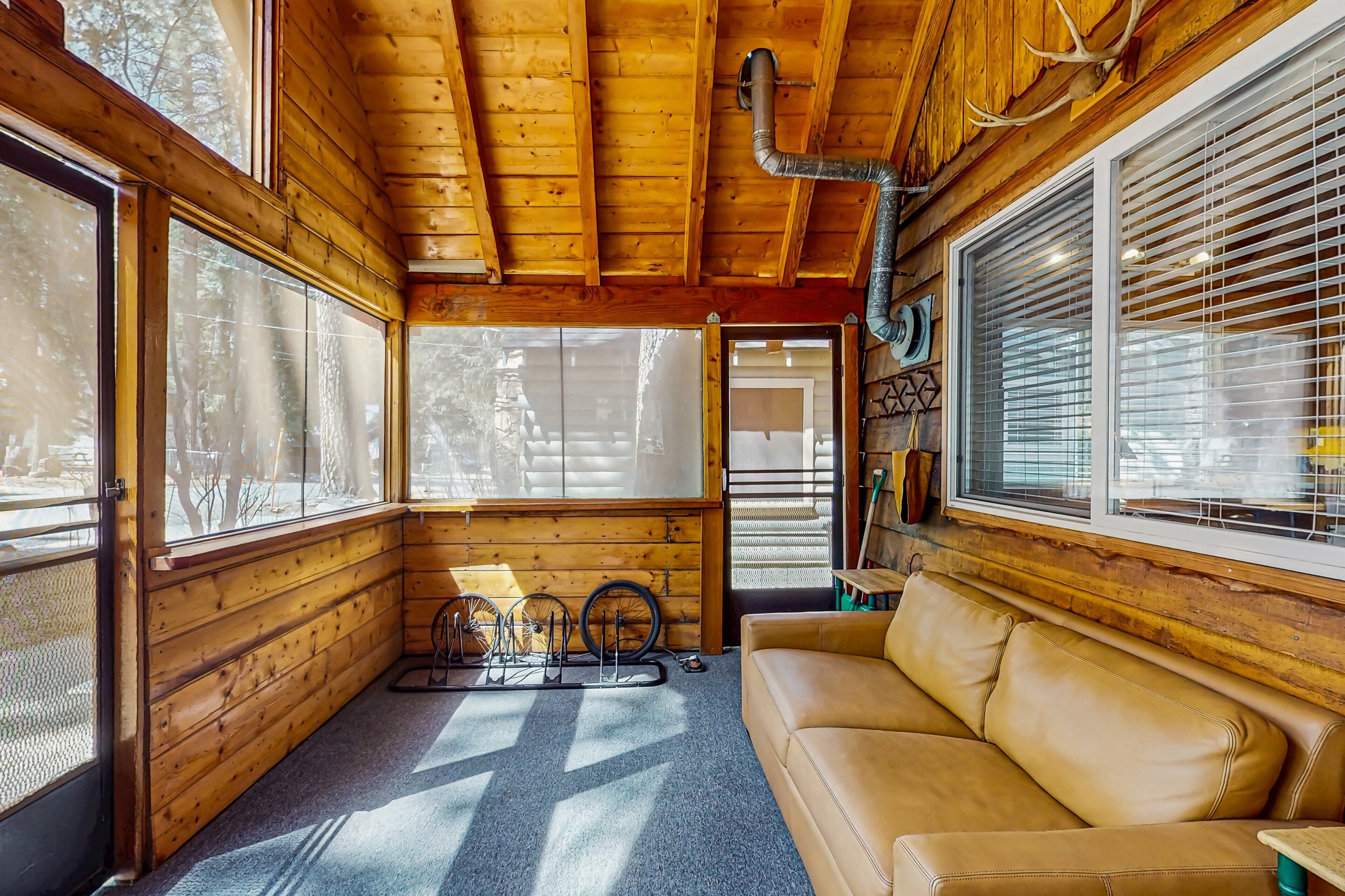 A cozy cabin interior with a leather couch, wooden walls, and large windows.