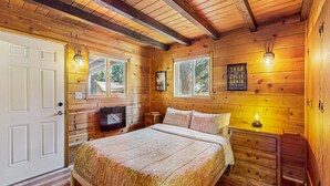 A wooden cabin bedroom with a bed, dresser, and a mounted television. - Bristlecone Cottage #321 (Big Bear Lake)