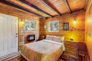 A wooden cabin bedroom with a bed, dresser, and a mounted television.